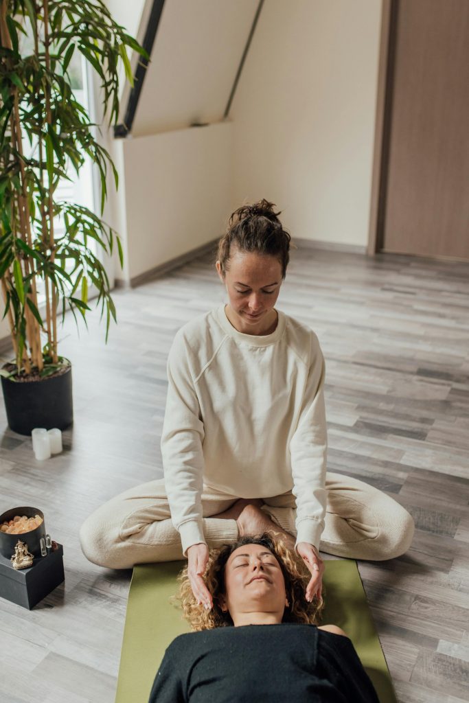 La praticienne reiki tient ses mains de chaque côté de la tête du receveur, concentrant l'énergie sur cette zone clé. Les paumes ouvertes dégagent une sensation de chaleur et de bien-être, symbolisant le transfert d'énergie visant à apaiser l'esprit et à clarifier les pensées. L'atmosphère est paisible, évoquant une profonde relaxation mentale et un rééquilibrage des énergies, contribuant à un état de tranquillité intérieure et de guérison émotionnelle.
